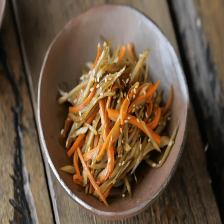 A delicious stir-fried burdock root (gobo) dish with carrots, sesame seeds, and a savory soy-based glaze, served as a Japanese side dish.