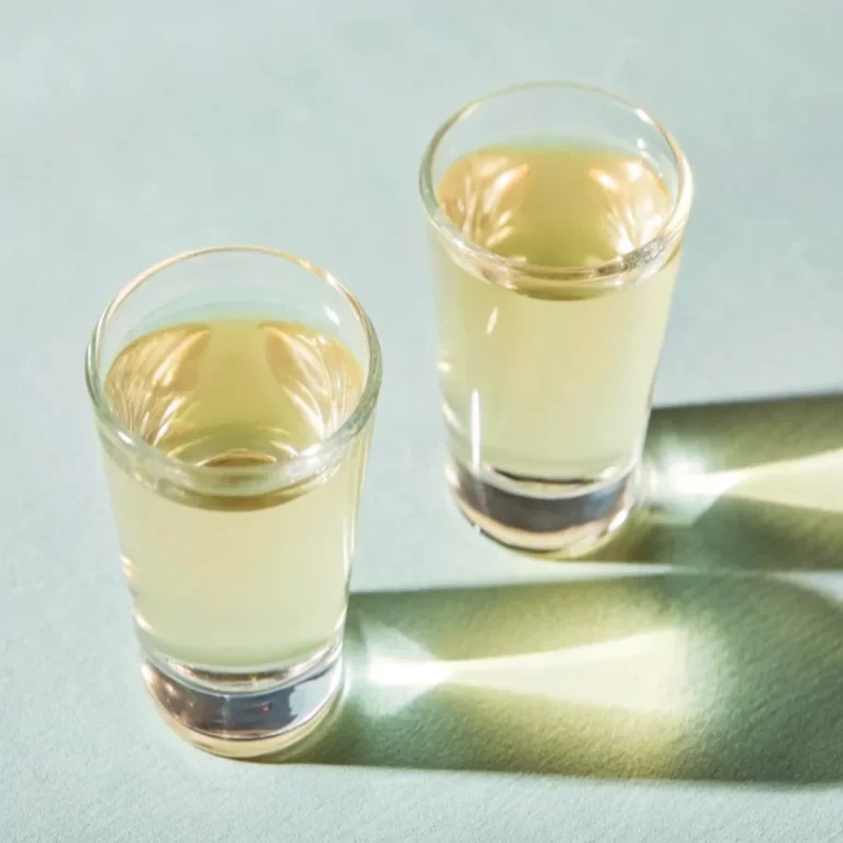 Green Tea Shot with whiskey, peach schnapps, and sour mix in shot glasses, garnished with a lemon wedge.