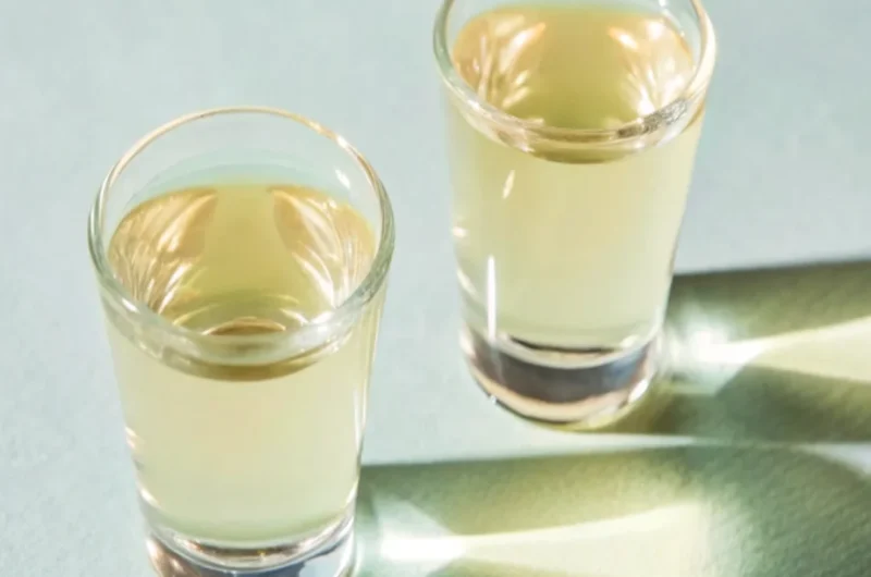 Green Tea Shot with whiskey, peach schnapps, and sour mix in shot glasses, garnished with a lemon wedge.