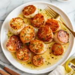 Perfect lemon butter scallops with golden sear served in a rich sauce on white plate with fresh herbs and gold fork.
