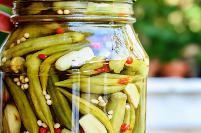Homemade pickled okra recipe in glass jar with spices and garlic cloves