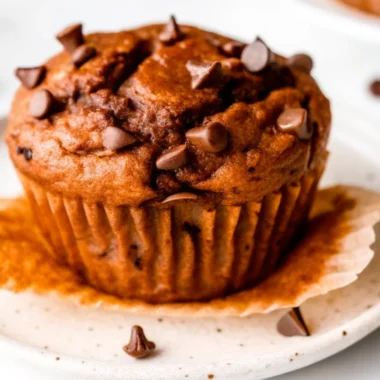 Close-up of a moist pumpkin protein muffin topped with chocolate chips on a ceramic plate.