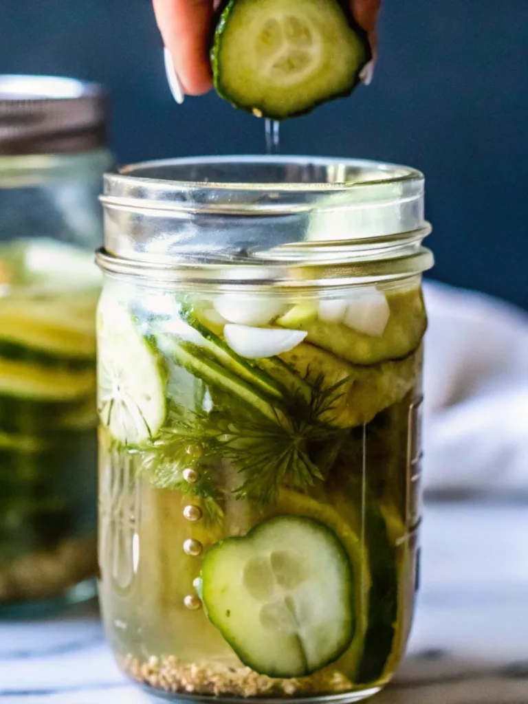 A close-up of a glass jar filled with freshly made refrigerator pickles, featuring sliced cucumbers, fresh dill sprigs, garlic cloves, and spices in a tangy brine—perfect for an easy dill pickles recipe.