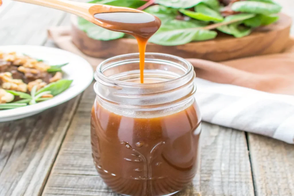 Homemade balsamic vinaigrette in a mason jar with salad and nuts in the background