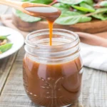 Homemade balsamic vinaigrette in a mason jar with salad and nuts in the background