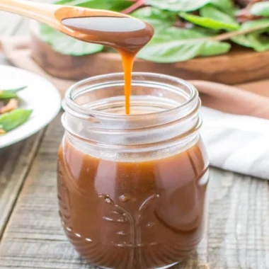 Homemade balsamic vinaigrette in a mason jar with salad and nuts in the background