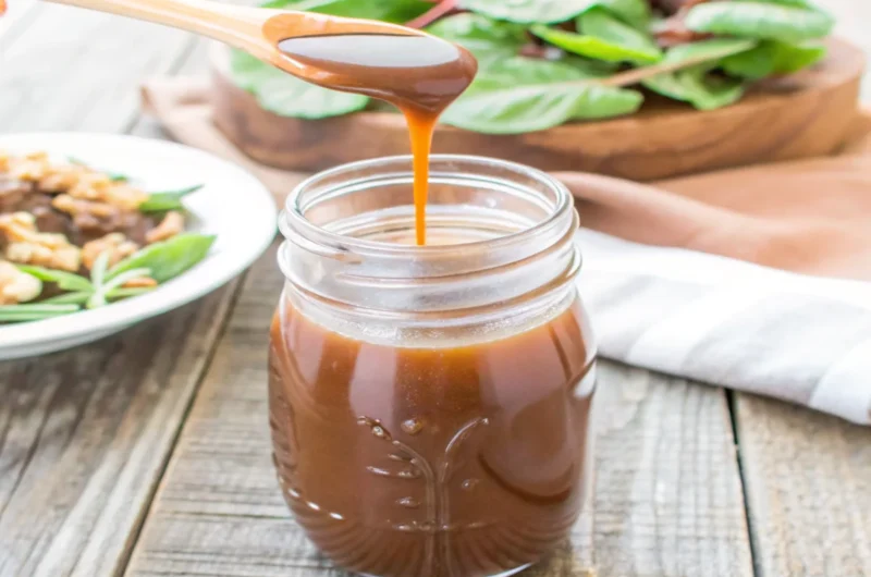 Homemade balsamic vinaigrette in a mason jar with salad and nuts in the background