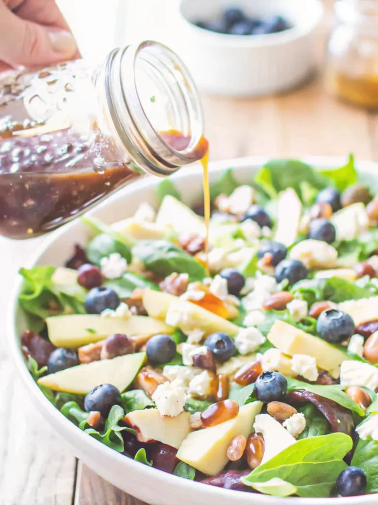 Homemade balsamic vinaigrette in a mason jar with salad and nuts in the background