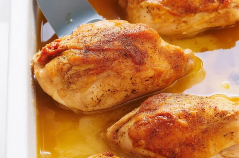 Juicy oven baked chicken breast with seasoning on a baking tray.