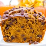 Sliced pumpkin chocolate chip bread with chocolate chips on white plate surrounded by orange pumpkins - homemade fall baking recipe