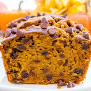 Sliced pumpkin chocolate chip bread with chocolate chips on white plate surrounded by orange pumpkins - homemade fall baking recipe