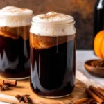 Glass of pumpkin spice cold brew topped with whipped foam and cinnamon, surrounded by pumpkins, cinnamon sticks, and star anise.