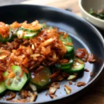 Close-up of a vibrant rispy rice salad featuring golden crispy baked rice atop fresh diced Persian cucumbers, chopped mint, spring onions, and a savory soy-ginger dressing in a black bowl.