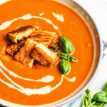 Roasted tomato soup with fresh tomatoes, creamy swirl, and crispy grilled cheese croutons topped with fresh basil.