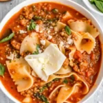 Hearty lasagna soup in a gray pot topped with melted cheese and fresh herbs, showcasing layers of pasta, ground beef, and creamy cheese blend