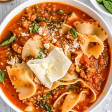 Hearty lasagna soup in a gray pot topped with melted cheese and fresh herbs, showcasing layers of pasta, ground beef, and creamy cheese blend