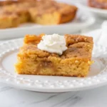 Slice of keto pumpkin cake with gooey butter topping on white plate with fork, showing moist texture and golden color