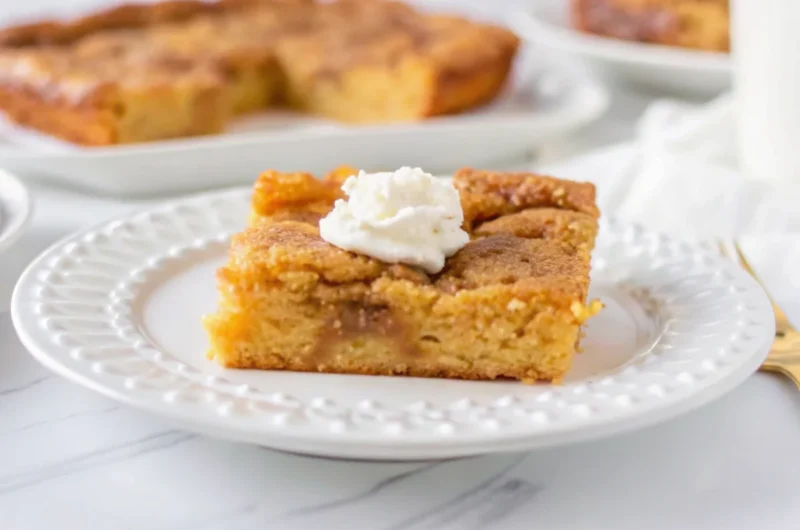 Slice of keto pumpkin cake with gooey butter topping on white plate with fork, showing moist texture and golden color
