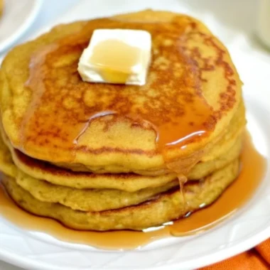 Fluffy golden low-carb pumpkin pancakes stacked on a white plate with butter and sugar-free syrup, showcasing this keto pumpkin recipe's perfect texture and autumn colors