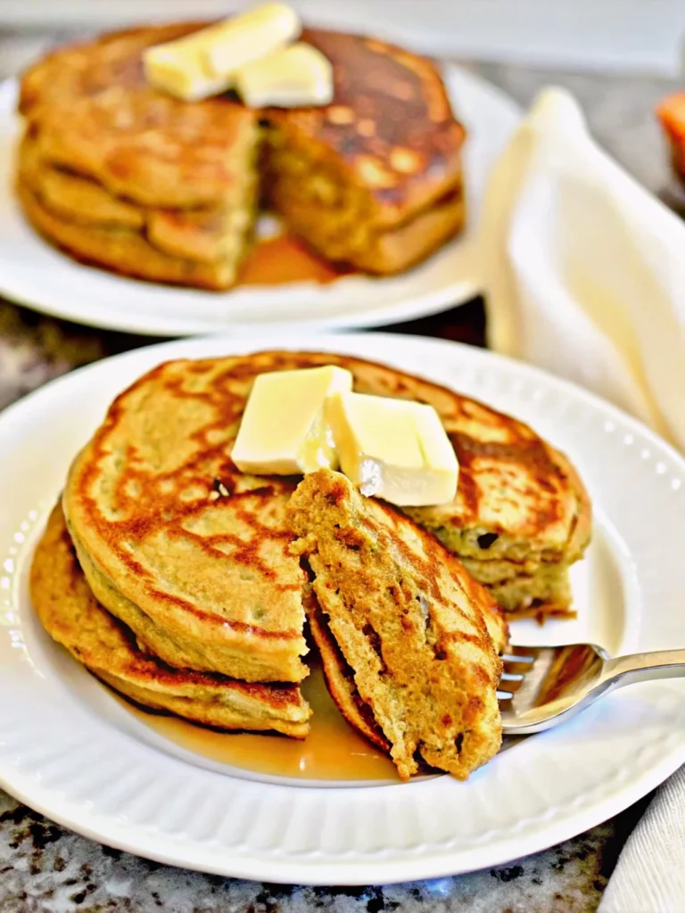 Fluffy golden low-carb pumpkin pancakes stacked on a white plate with butter and sugar-free syrup, showcasing this keto pumpkin recipe's perfect texture and autumn colors