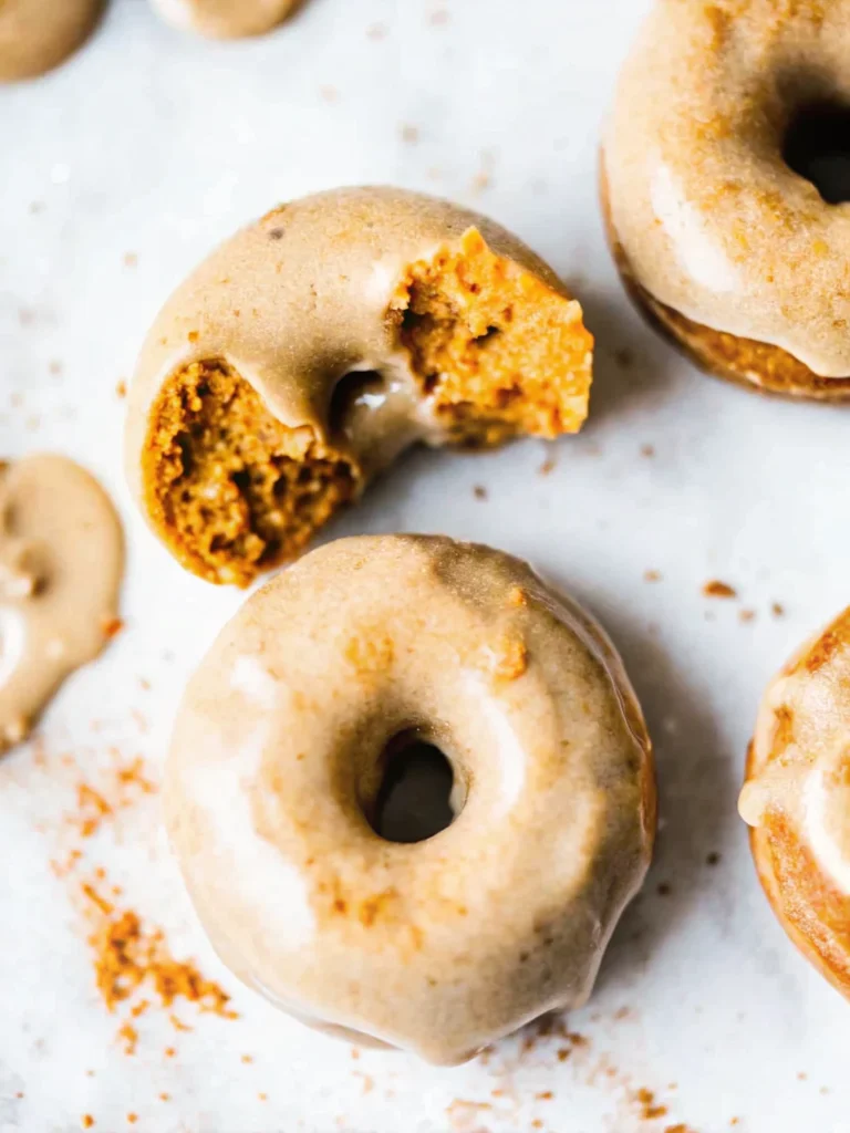 Freshly baked pumpkin donuts with maple glaze on cooling rack, golden brown color, fall baking recipe
