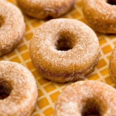 Golden brown baked pumpkin donuts coated in cinnamon sugar arranged on white plate with fall decorations