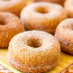 Golden brown baked pumpkin donuts coated in cinnamon sugar arranged on white plate with fall decorations
