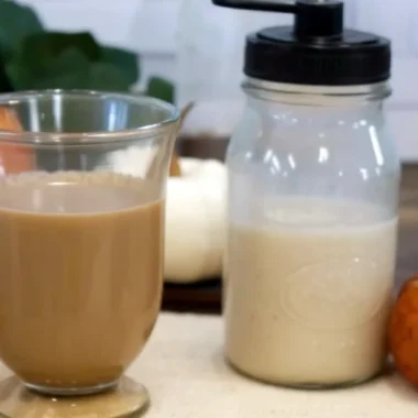 Homemade pumpkin creamer being poured into a white coffee mug with steam rising, showing the rich orange color and creamy texture of the fall-spiced coffee additive