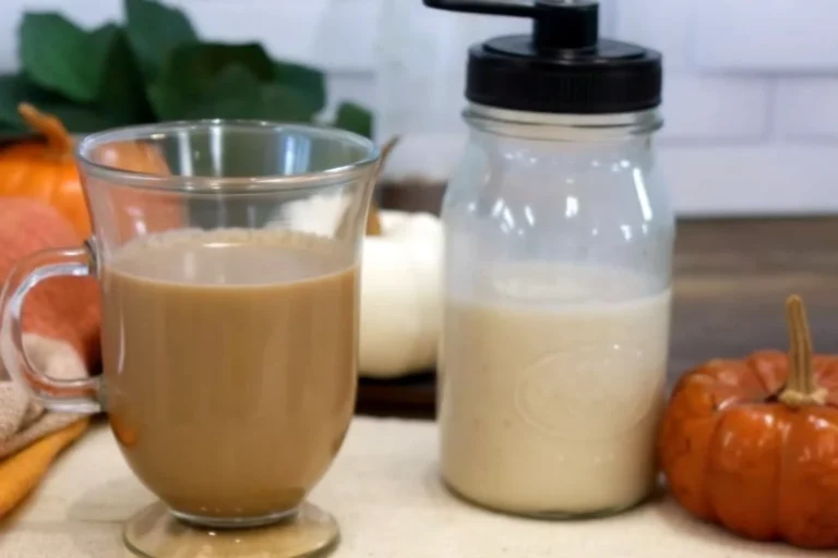 Homemade pumpkin creamer being poured into a white coffee mug with steam rising, showing the rich orange color and creamy texture of the fall-spiced coffee additive