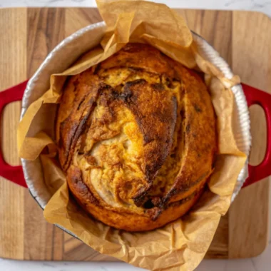 Golden pumpkin sourdough bread loaf with cranberries and pumpkin pie spice, sliced on wooden cutting board showing orange-colored crumb structure