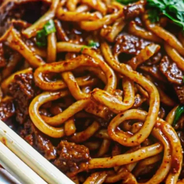 Quick and flavorful beef black pepper udon noodles with tender beef slices and crisp vegetables in glossy black pepper sauce served in white bowl