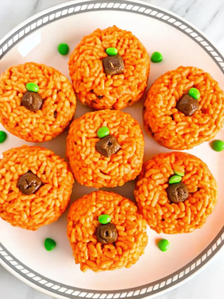 Orange pumpkin-shaped Rice Krispie treats with brown Tootsie Roll stems and green M&M leaves arranged on white background for Halloween party dessert