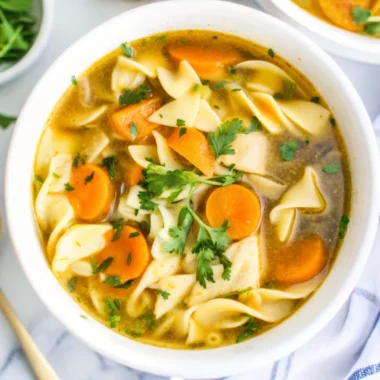Easy homemade chicken noodle soup with egg noodles in white bowl with fresh parsley garnish and crusty bread