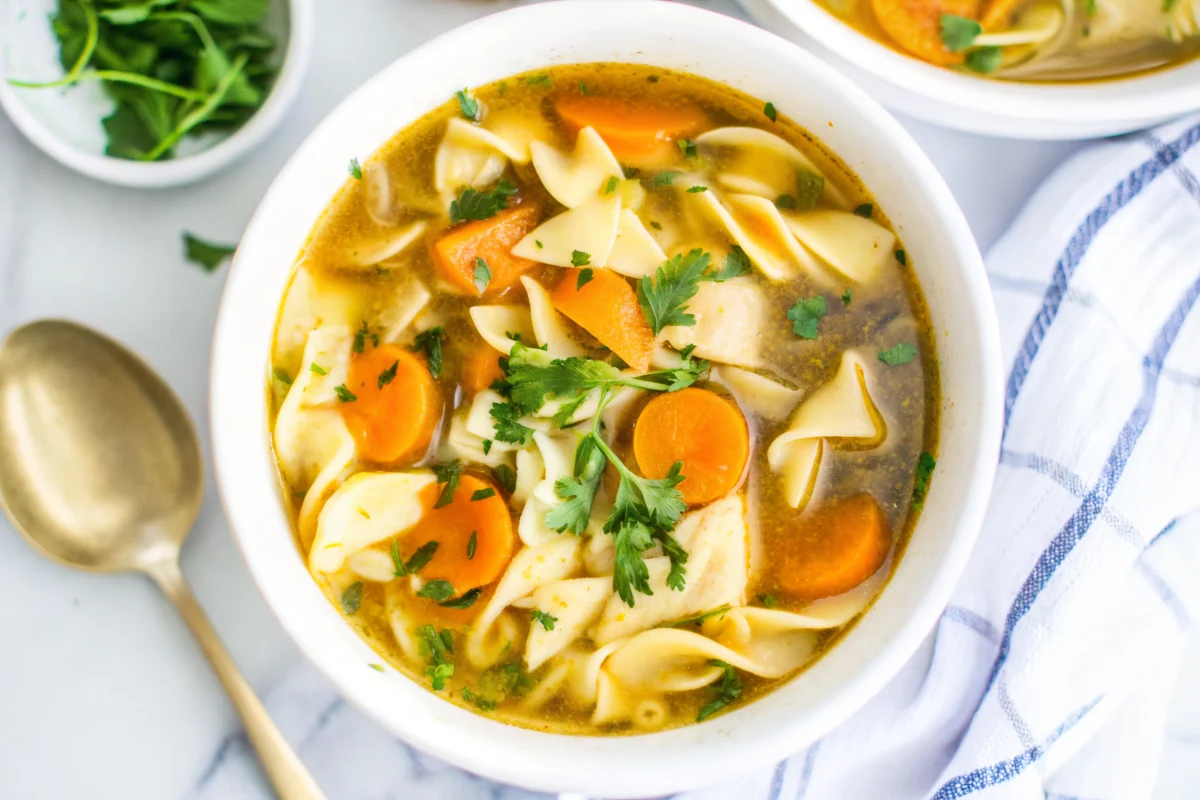 Easy homemade chicken noodle soup with egg noodles in white bowl with fresh parsley garnish and crusty bread