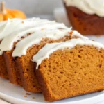 Sliced pumpkin bread with cream cheese frosting showing moist orange interior texture and white glaze drizzle