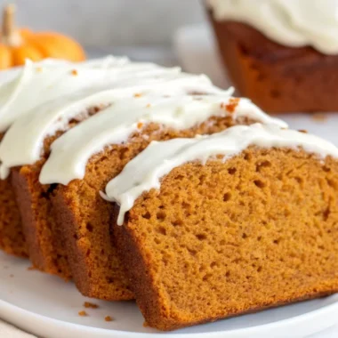 Sliced pumpkin bread with cream cheese frosting showing moist orange interior texture and white glaze drizzle