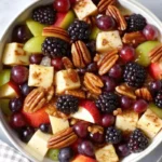 Colorful fall fruit salad with diced apples, pears, grapes, and pomegranate seeds in a wooden bowl, drizzled with maple cinnamon dressing and topped with toasted pecans