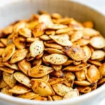 Golden brown salted roasted pumpkin seeds spread on parchment paper baking sheet, perfectly crispy pumpkin seeds recipe